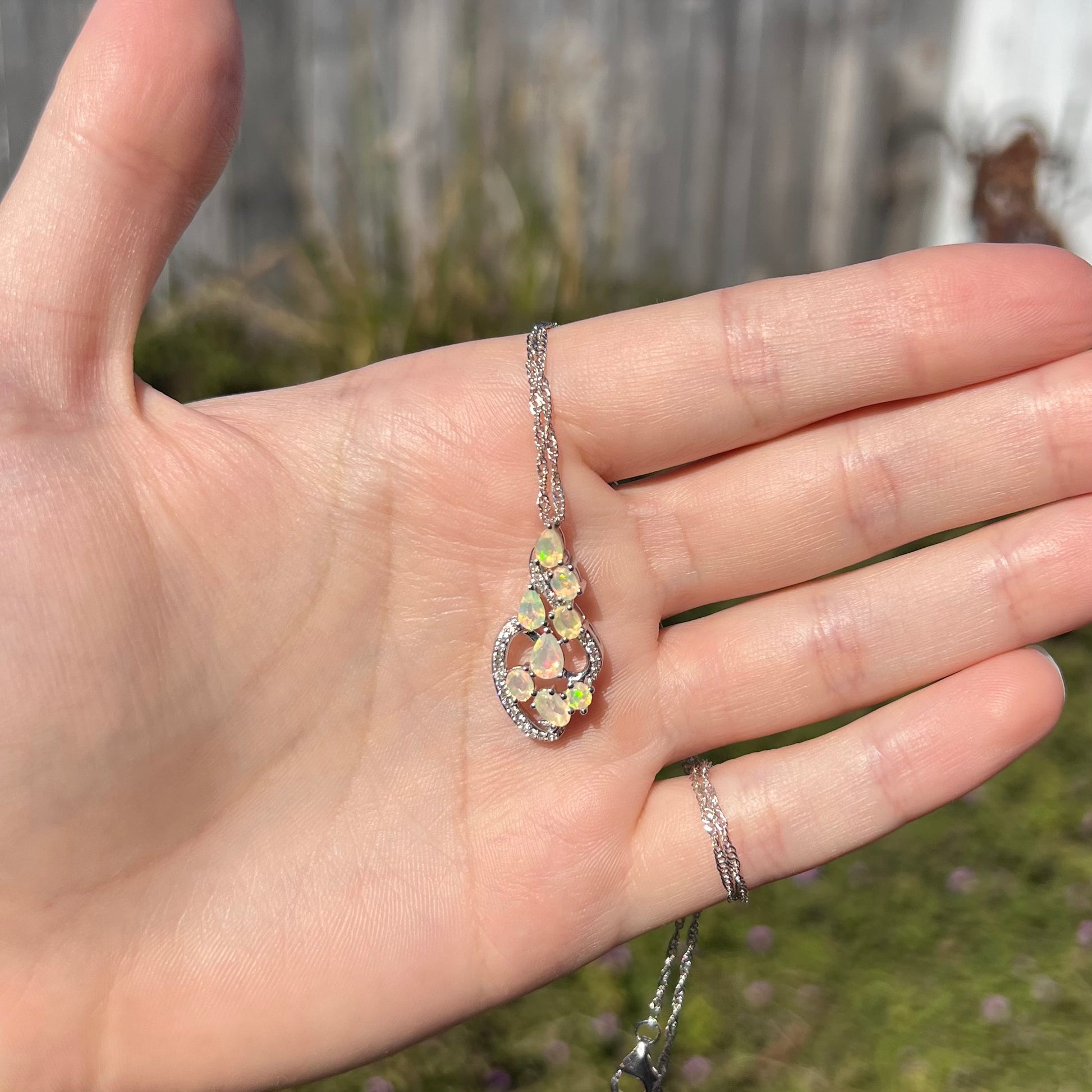 A sterling silver Ethiopian opal necklace held in a hand, shown in the sunlight.