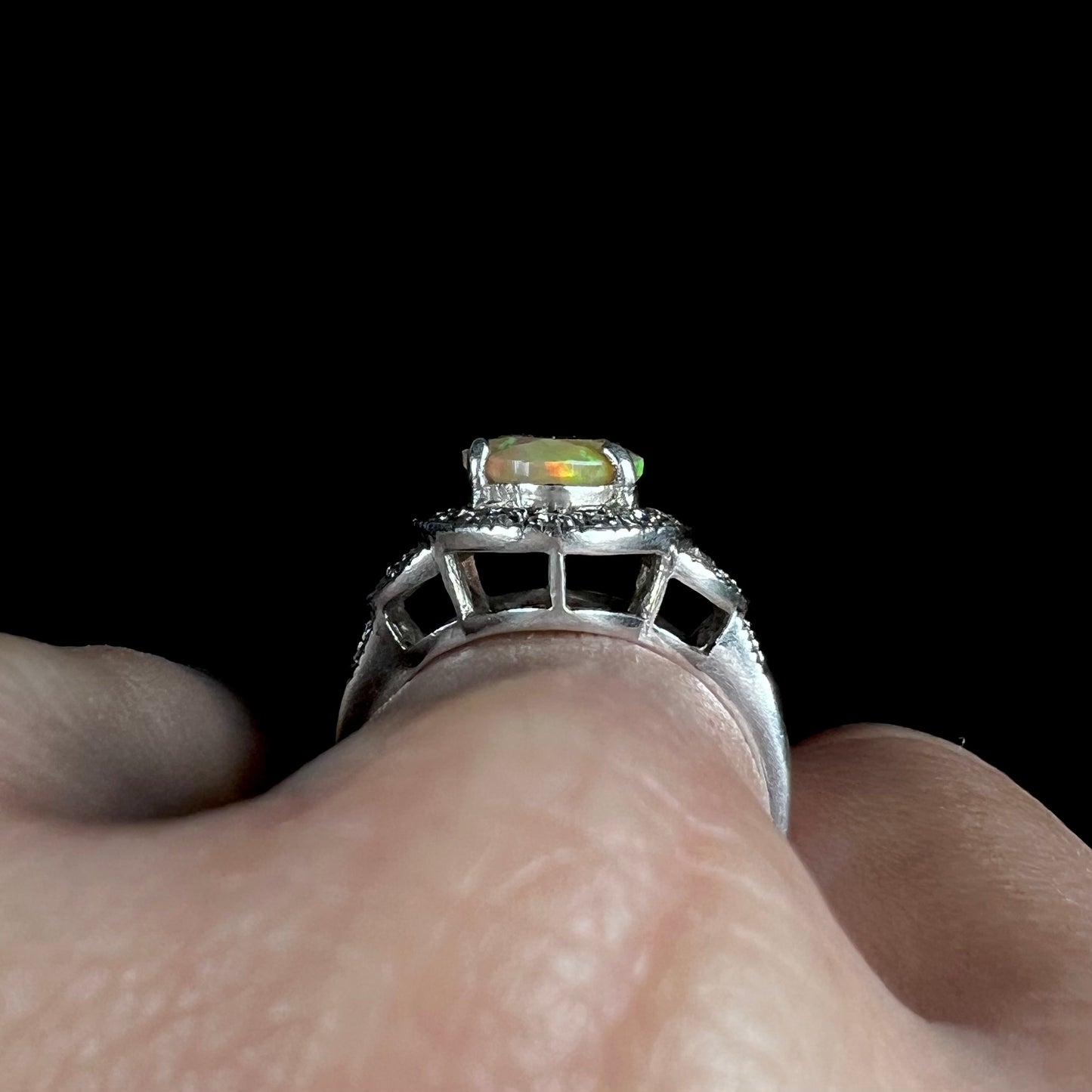 Close-up side gallery view of a silver Ethiopian opal ring worn on a hand against a black background.