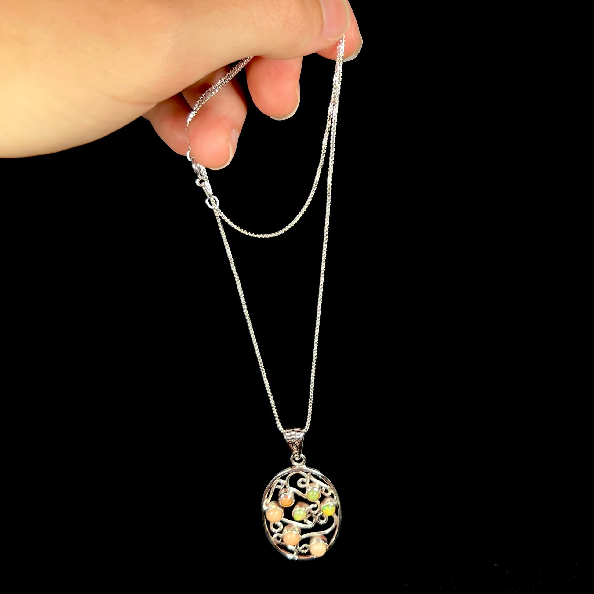 A sterling silver filigree Ethiopian opal necklace, dangling from a chain by its box-style chain.