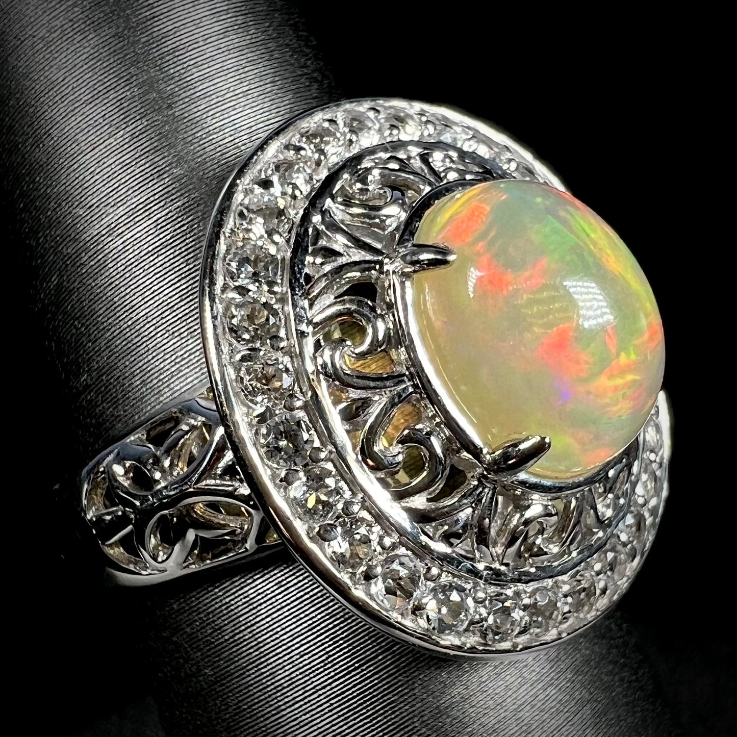 Angled view of silver filigree Ethiopian opal halo ring with white topaz accents.
