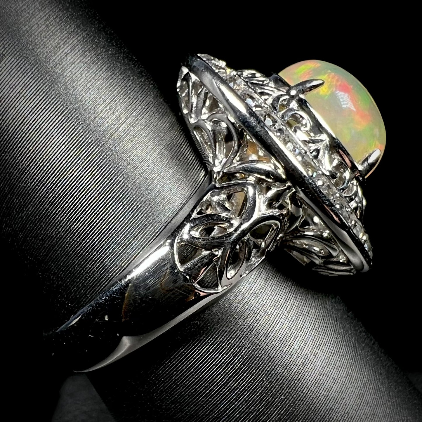 Side view of silver filigree opal ring against a black background.