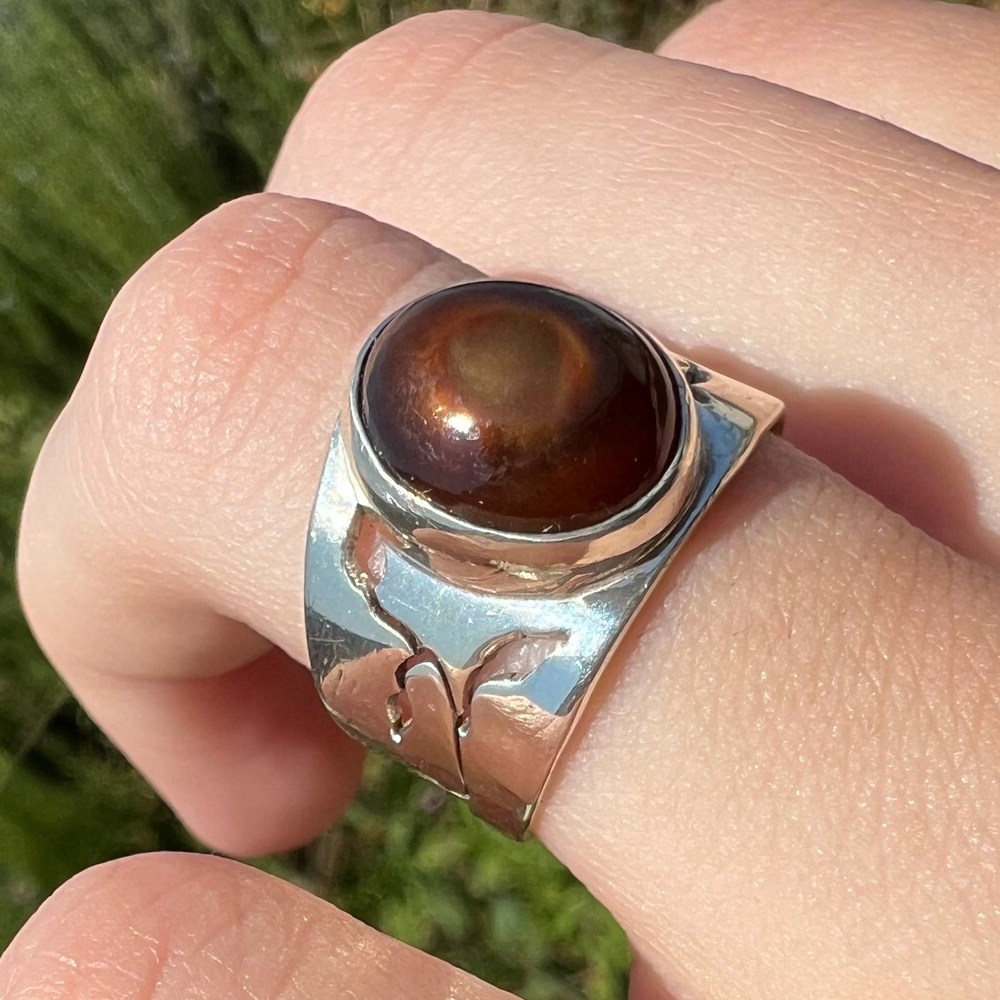 Close-up angled view of a silver fire agate ring worn on a finger in the sun. The fire agate is brown.