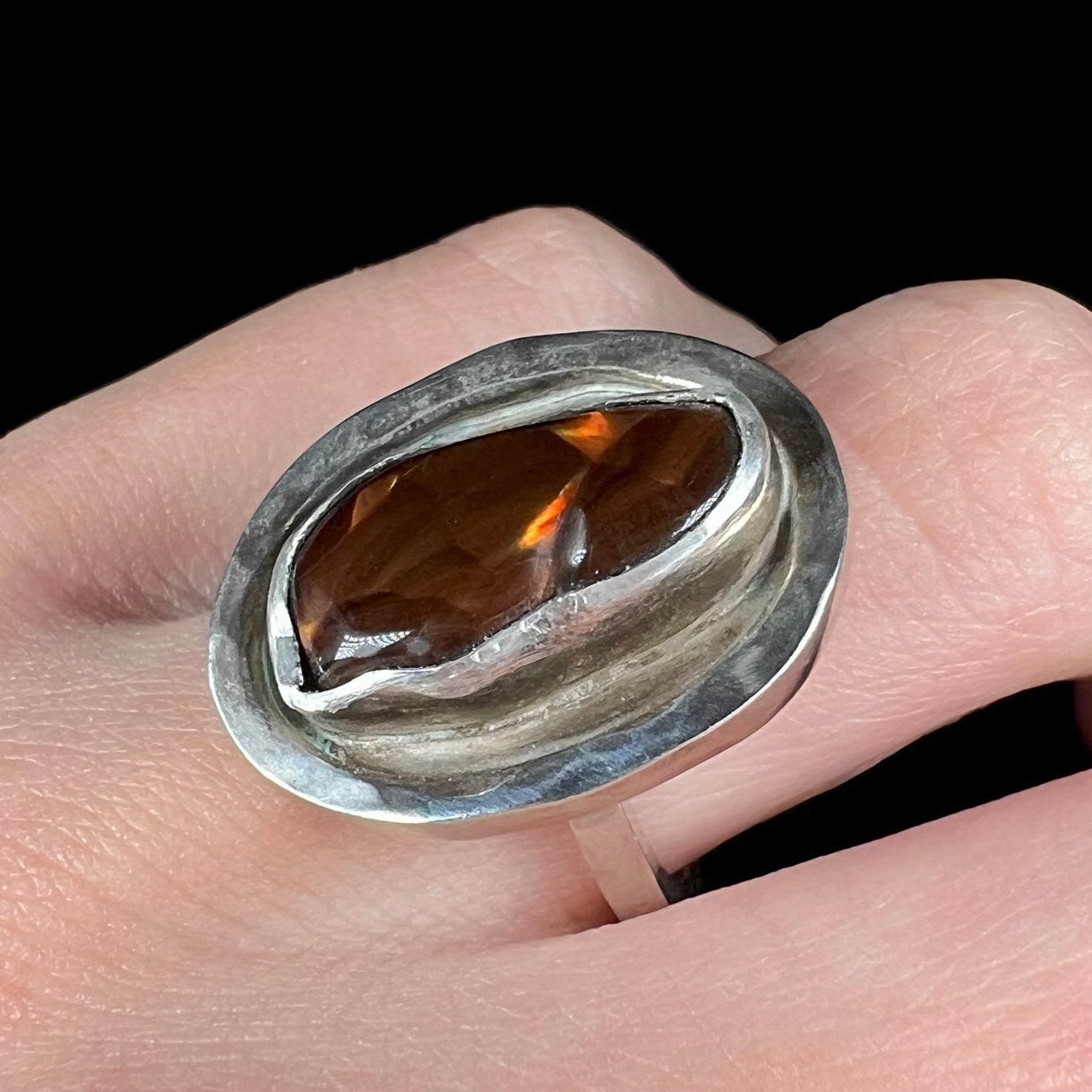 A handmade sterling silver fire agate ring worn on a finger, shown from an angle.