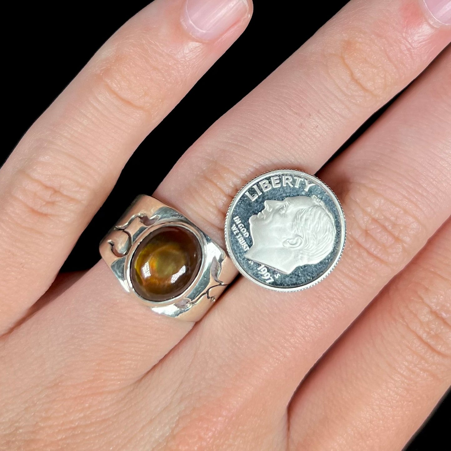 A sterling silver fire agate ring with an open vine design, worn on a hand next to a 1997 S dime coin.