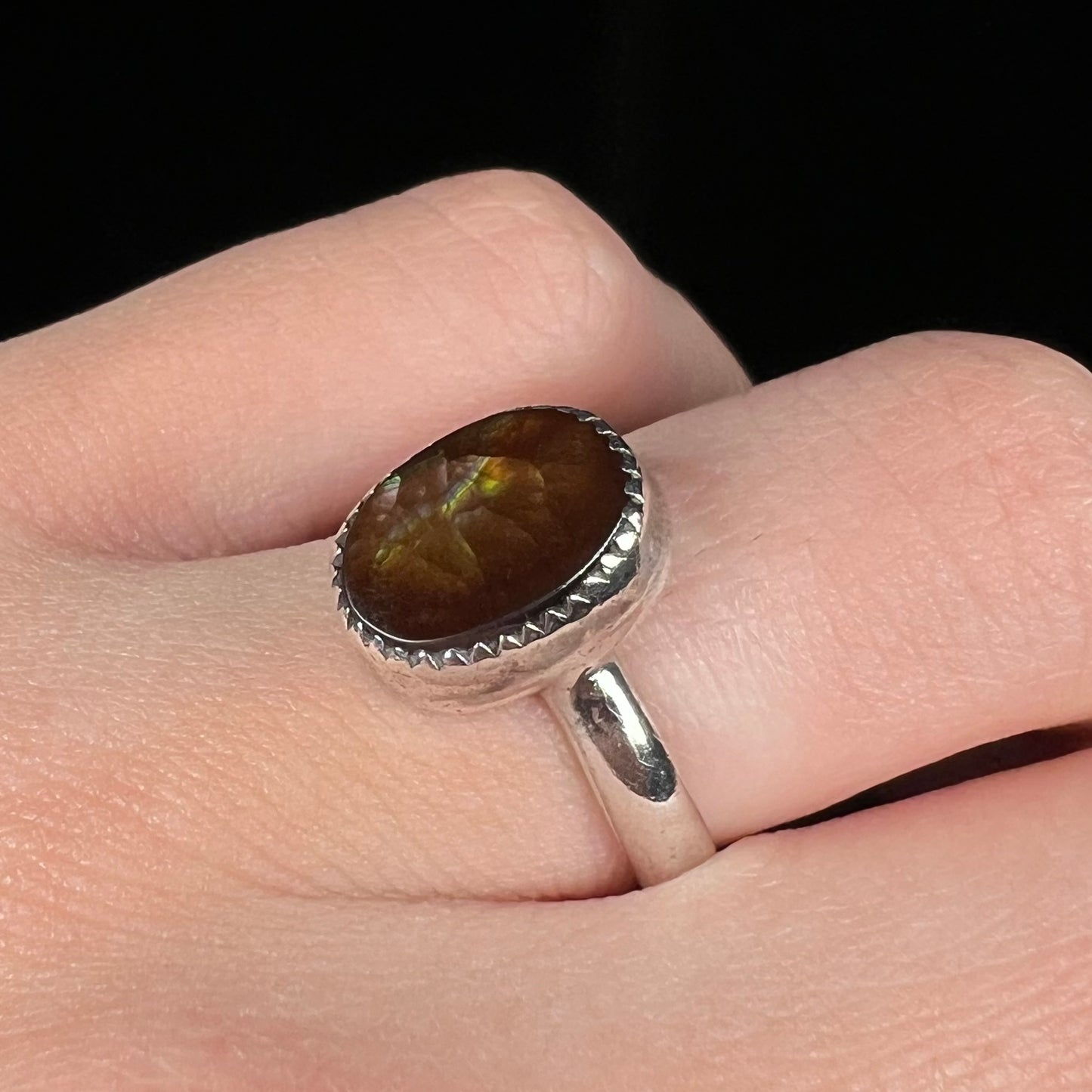 Macro angled view of finger wearing a silver fire agate ring against a black background.