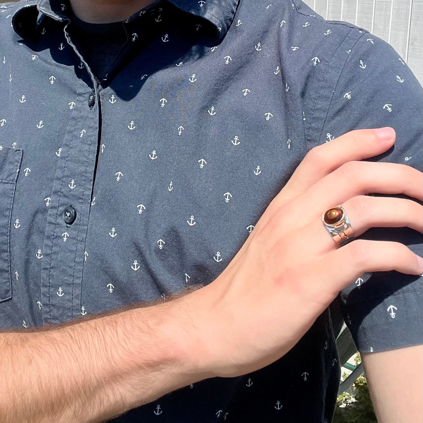 A model wearing a silver fire agate ring on his hand while resting his hand on his opposing shoulder.