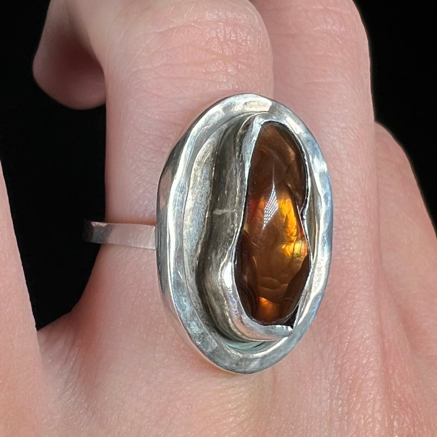Angled view of a handmade sterling silver fire agate ring, worn on a finger.
