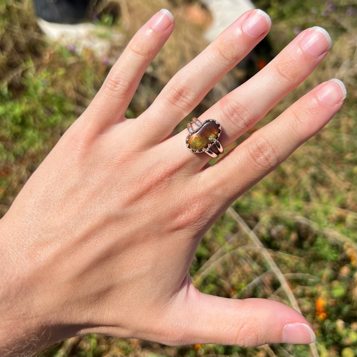 Hand wearing a silver fire agate ring in the sunlight against outdoor backdrop. The fire agate appears green.