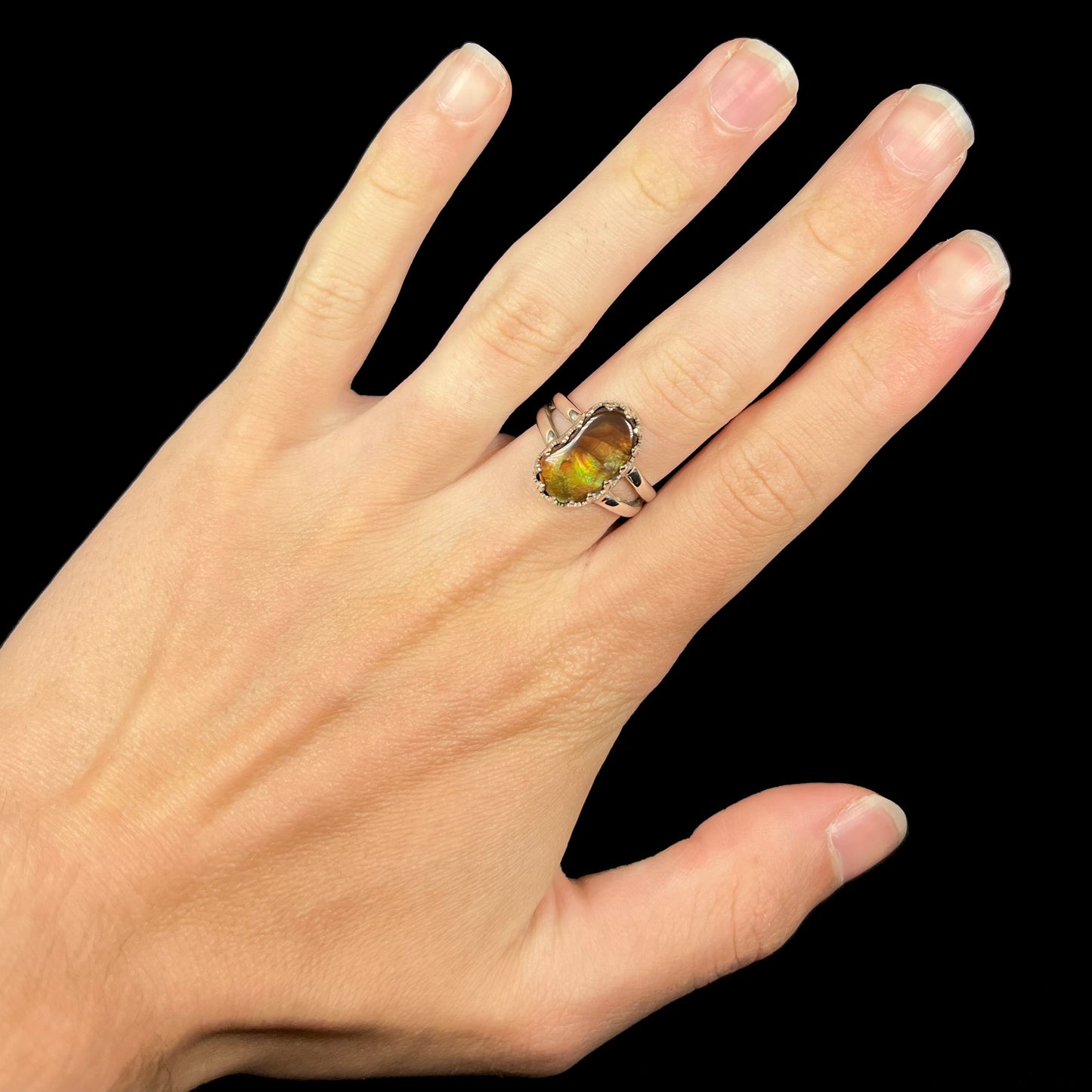 Hand wearing a freeform shaped silver Mexican fire agate ring against black background.