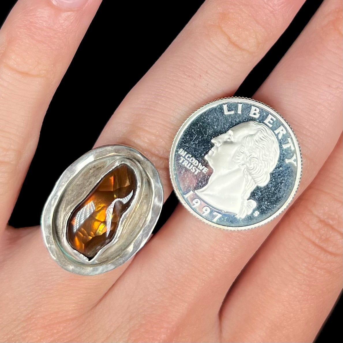 A handmade sterling silver fire agate ring worn on a hand next to a 1997 S quarter coin.