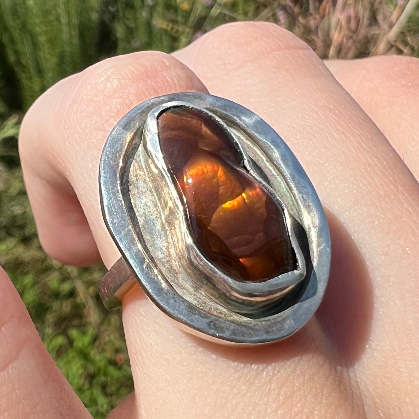 Angled sunlit view of a handmade sterling silver fire agate ring, worn on a finger.