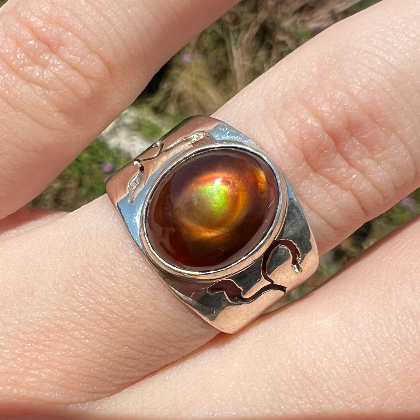 A sterling silver fire agate ring shown on a finger in the sunlight close-up from its front.