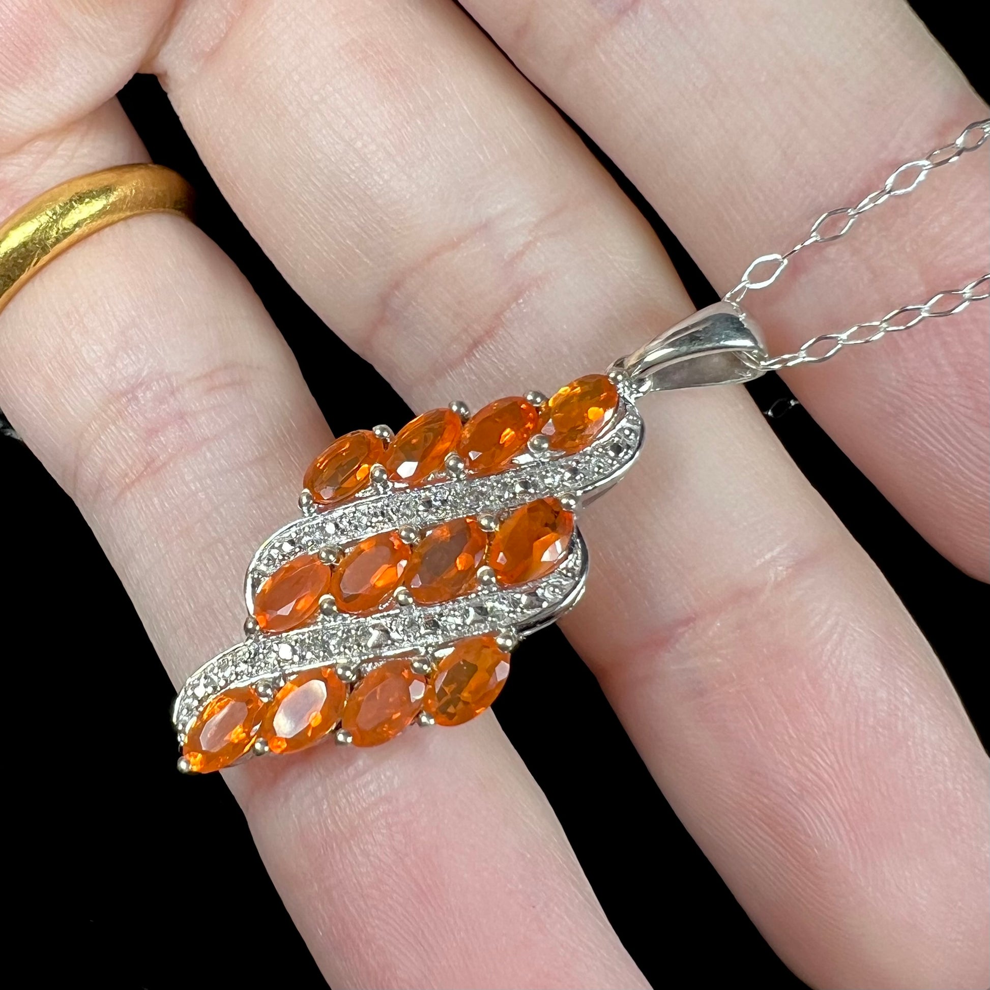 A silver fire opal cluster pendant featuring faceted orange Mexican opals held in a hand at an angle.