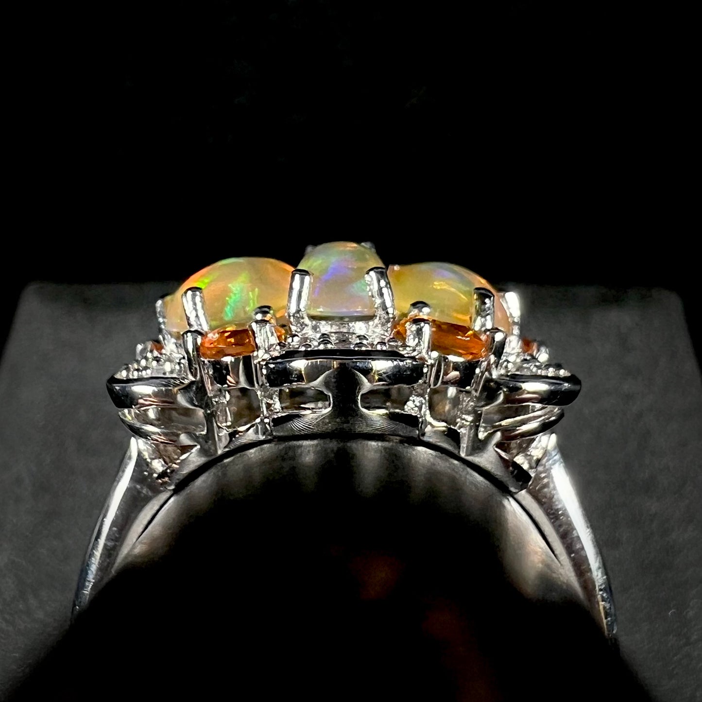 Side gallery profile view of a sterling silver fire opal cluster ring against a black and gray backdrop.