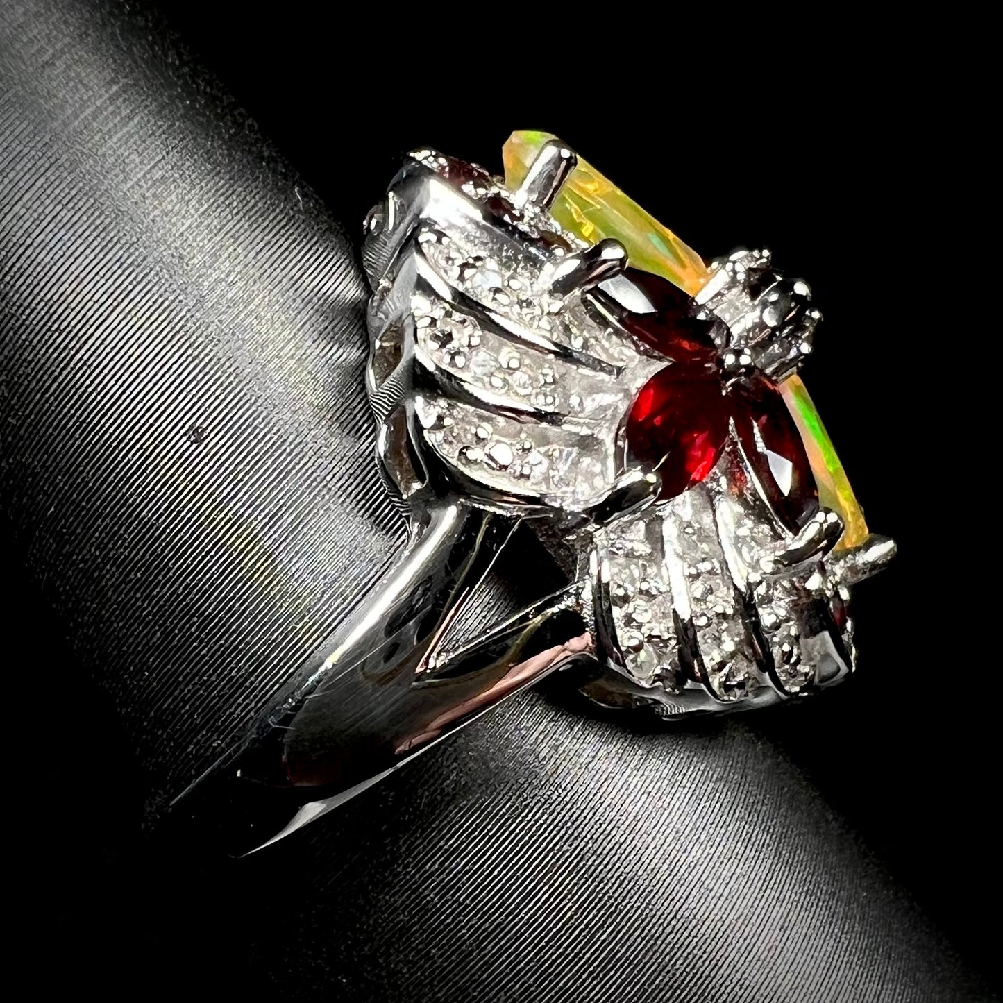 A silver garnet and opal ring with diamond accents, shown from the side view.