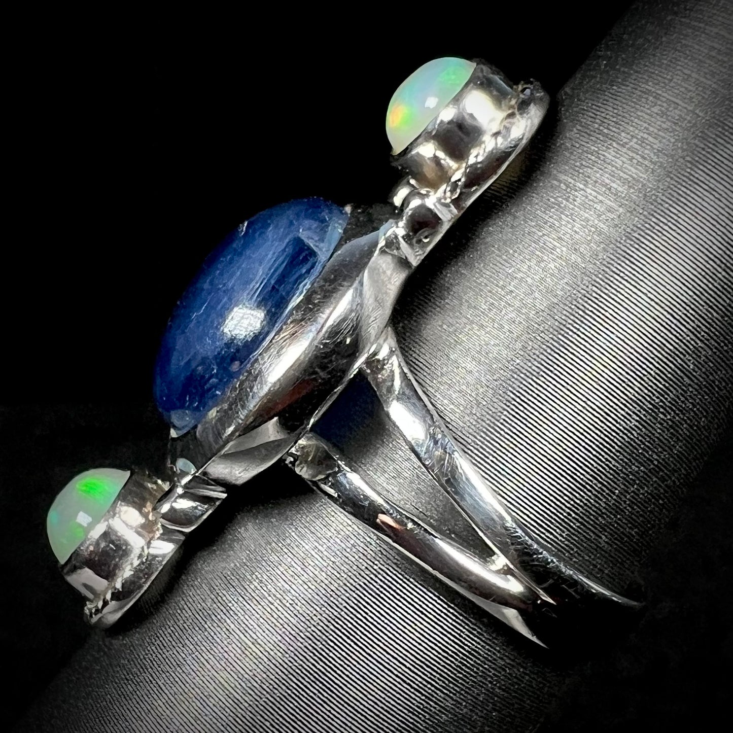 Side view of a silver kyanite and opal ring against a black background. The ring's split shank is in focus.