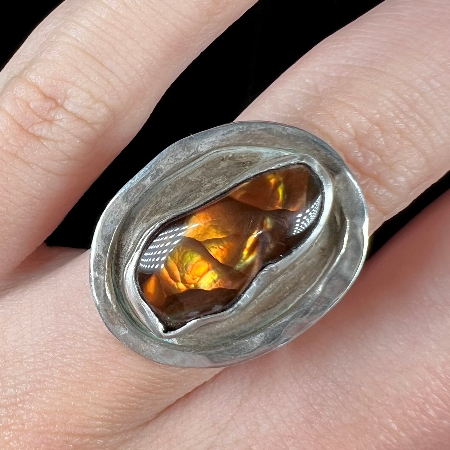 Close-up of a handmade sterling silver Mexican fire agate ring, worn on a finger.