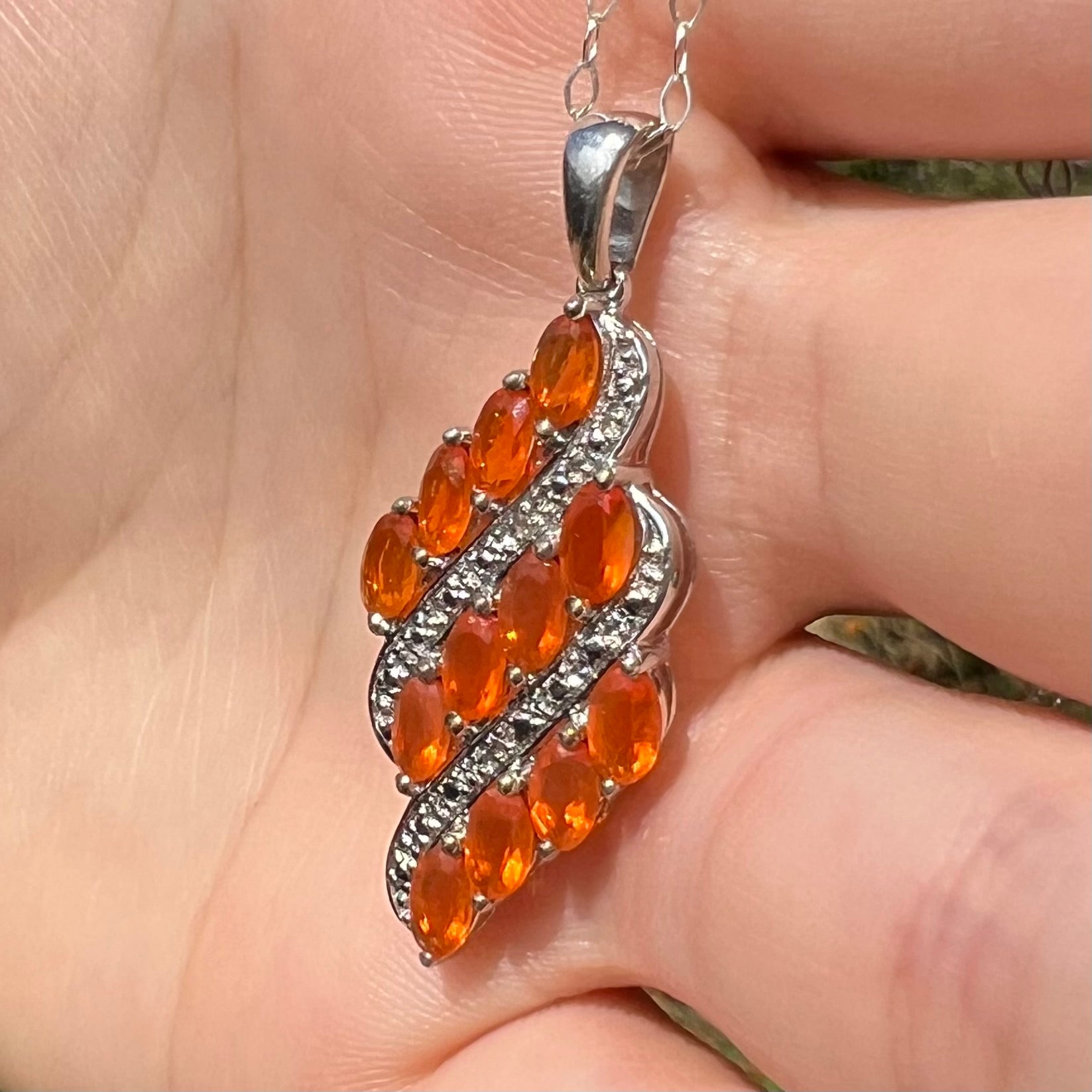 A silver Mexican fire opal necklace featuring a cluster of faceted orange fire opals, shown at an angle in sunlight.