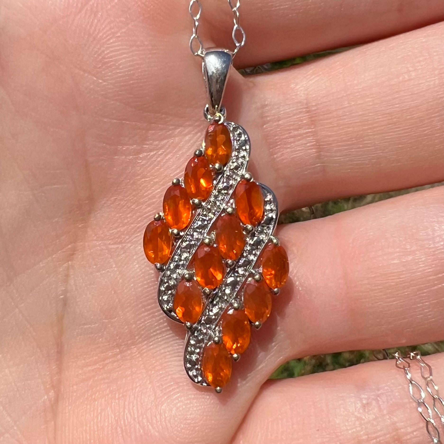 Close-up of a silver Mexican fire opal pendant, held in a hand in natural sunlight.