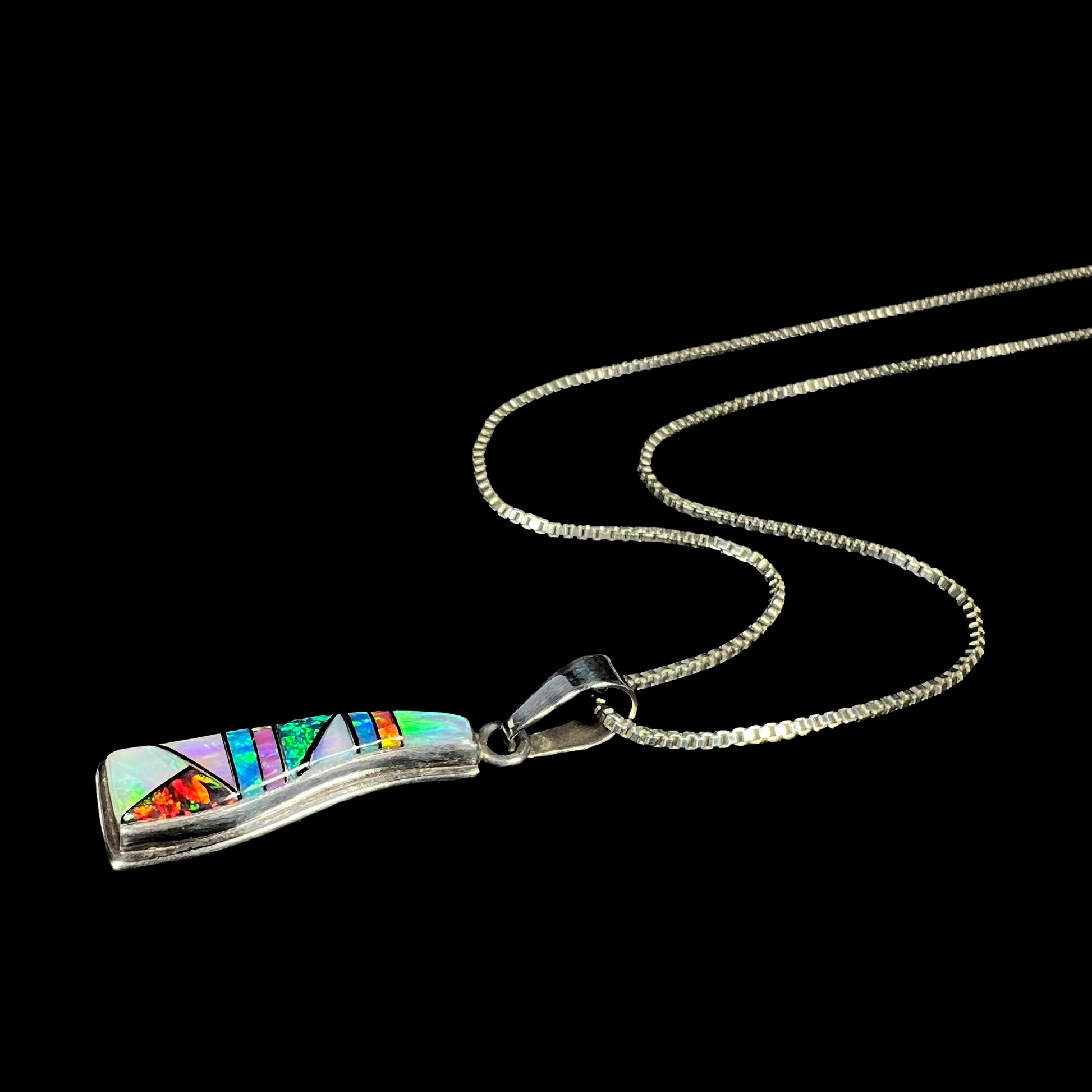 A sterling silver Navajo-made opal inlay necklace shown laying at an angle against a black background.