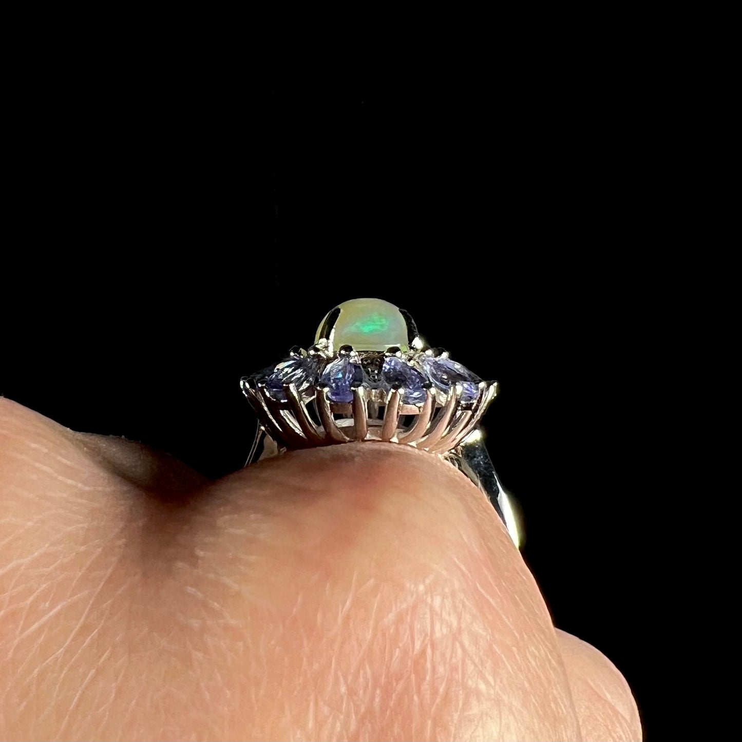 Side basket view of a silver opal ring, worn on a hand against a black backdrop.