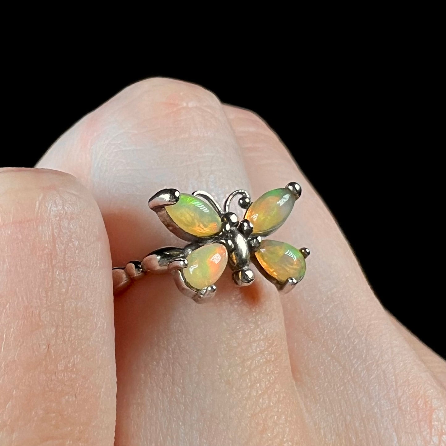 A sterling silver Ethiopian opal butterfly ring shown close-up at an angle on a finger against a black background.