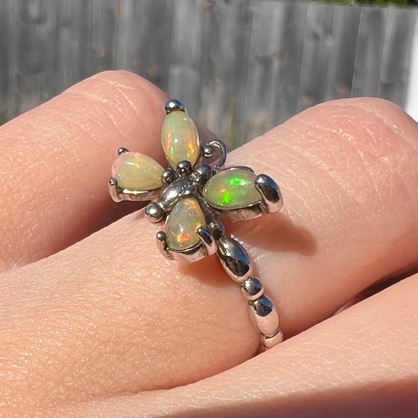 Close-up angled view of a sterling silver Ethiopian opal butterfly ring worn on a finger in sunlight.