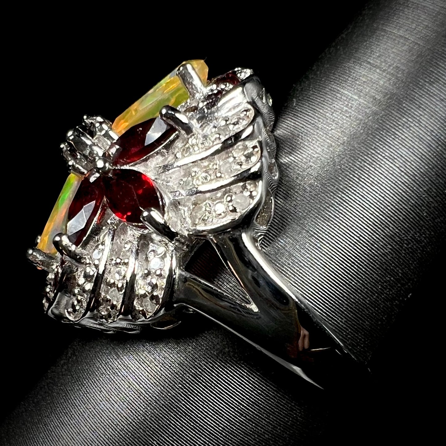 Side view of a silver opal, diamond, and garnet ring, showing the ring's split shank design.