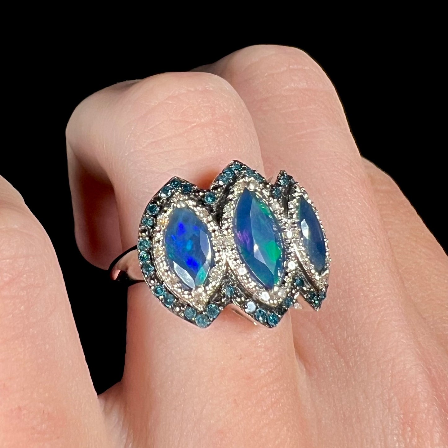 A silver opal and diamond ring, featuring blue opals and blue diamonds, worn on a finger at an angle.