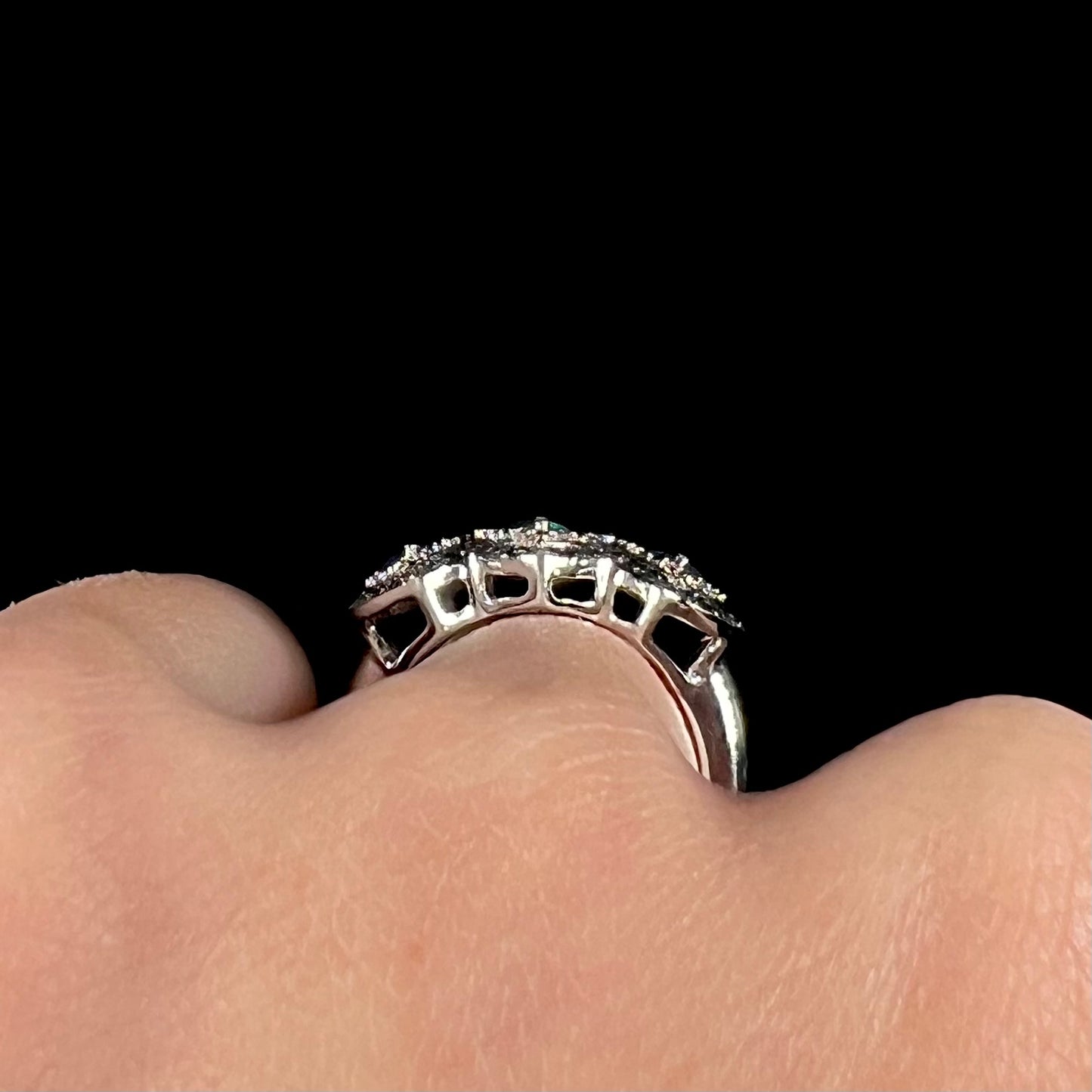 Side gallery view of a sterling silver opal and diamond ring worn on a hand against a black background.