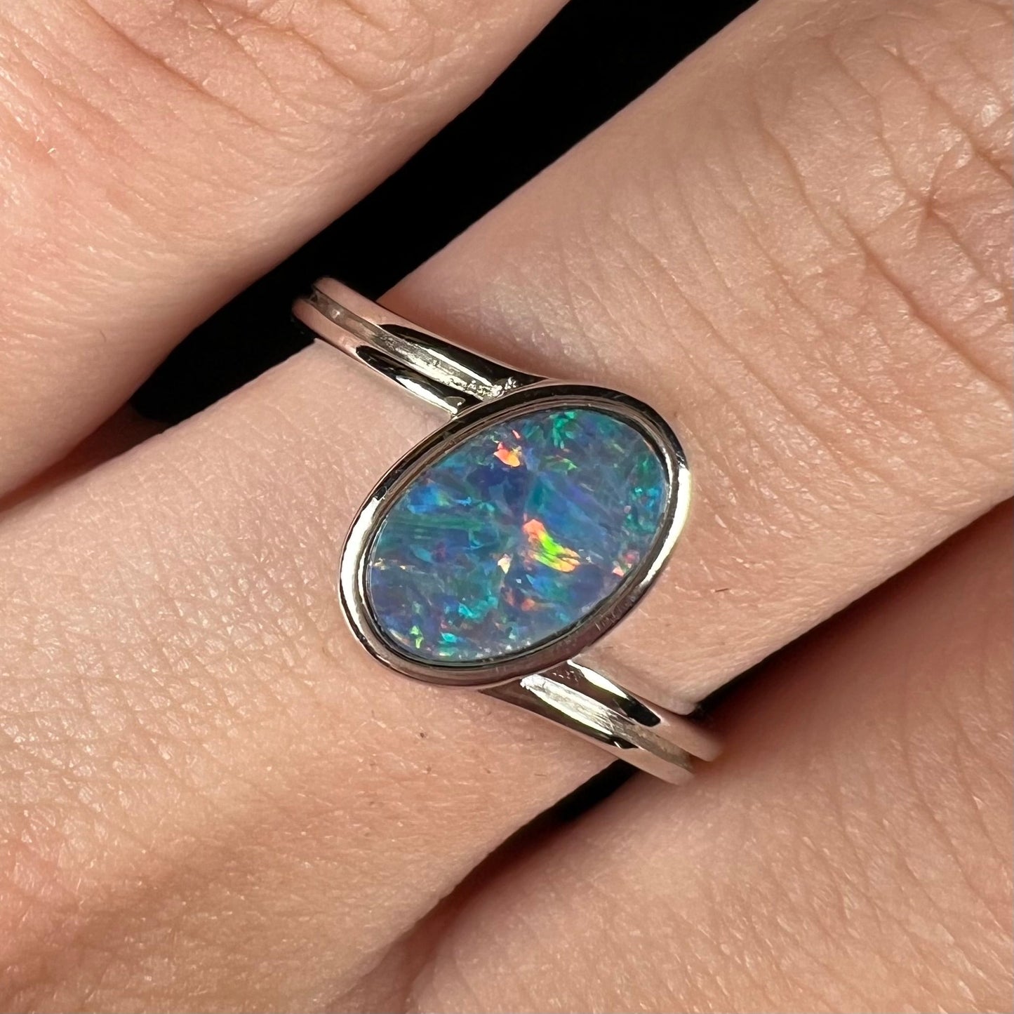 A sterling silver ring bezel-set with an oval shaped black opal doublet. The opal has red and blue fire.