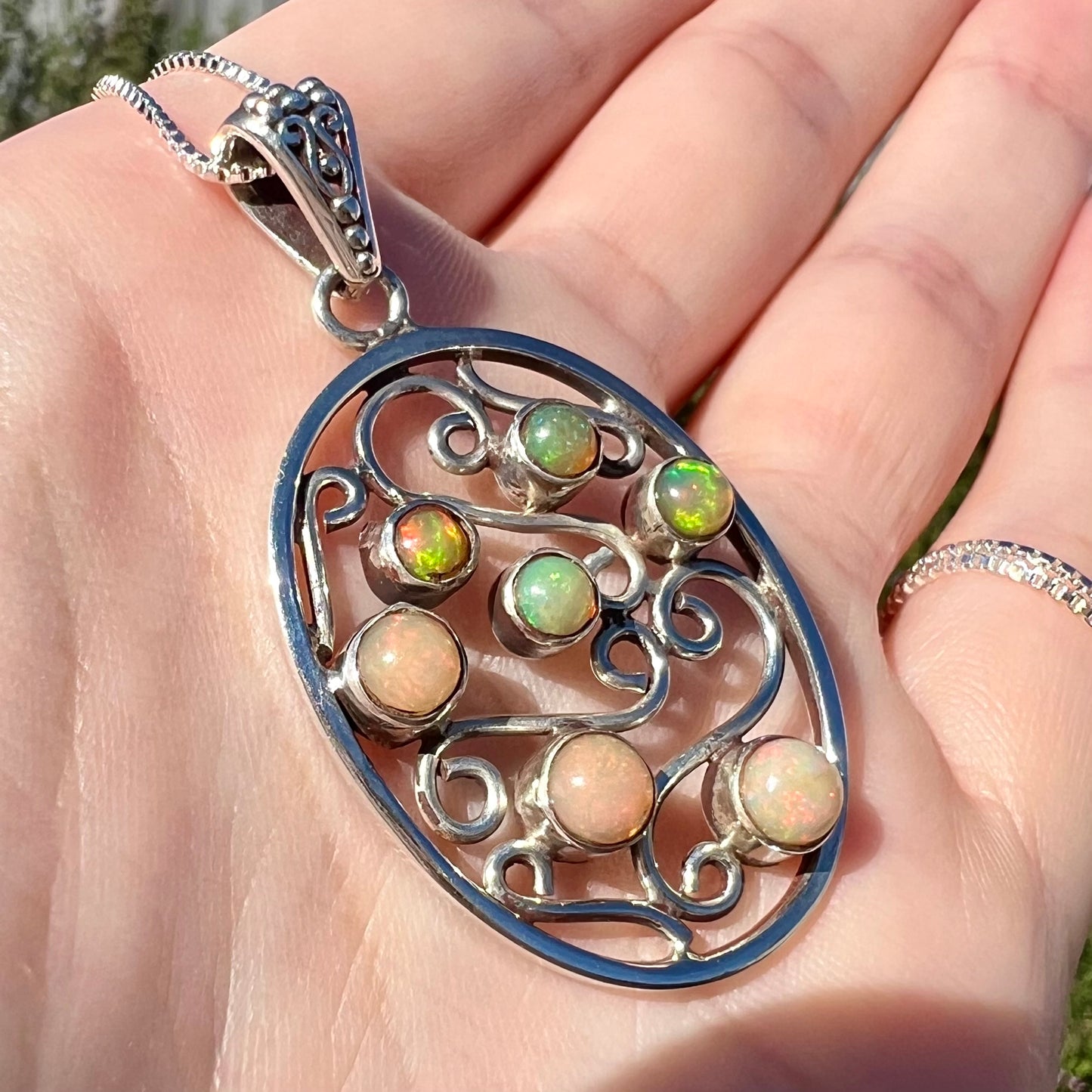 A sterling silver Ethiopian opal filigree necklace shown at an angle close-up in a hand in sunlight.