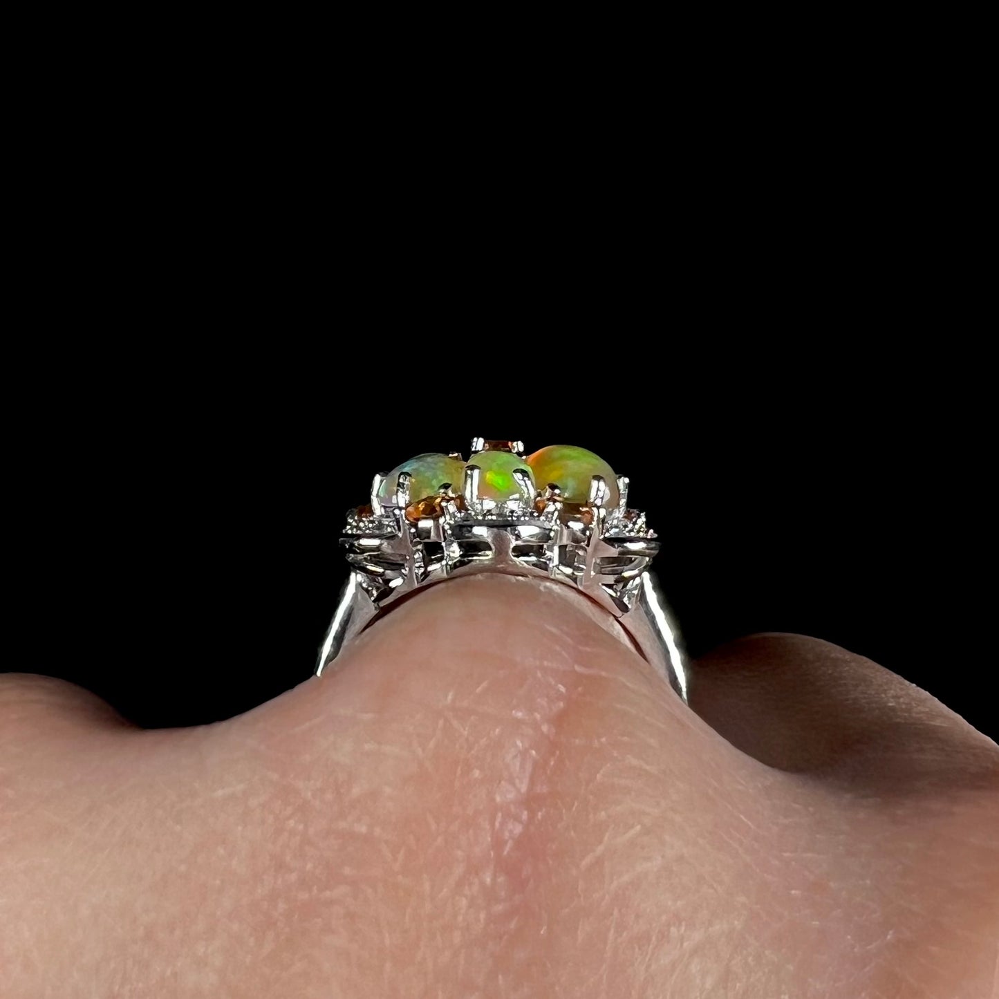 Side profile gallery view of a silver opal flower ring worn on a hand against a black background.