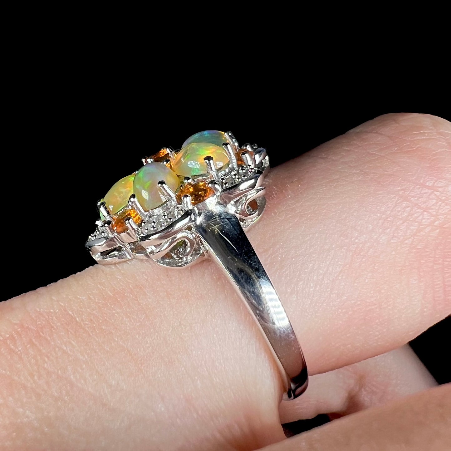 The side of a silver opal flower ring worn on a finger, focused on an eye-visible scratch on the ring's shank.