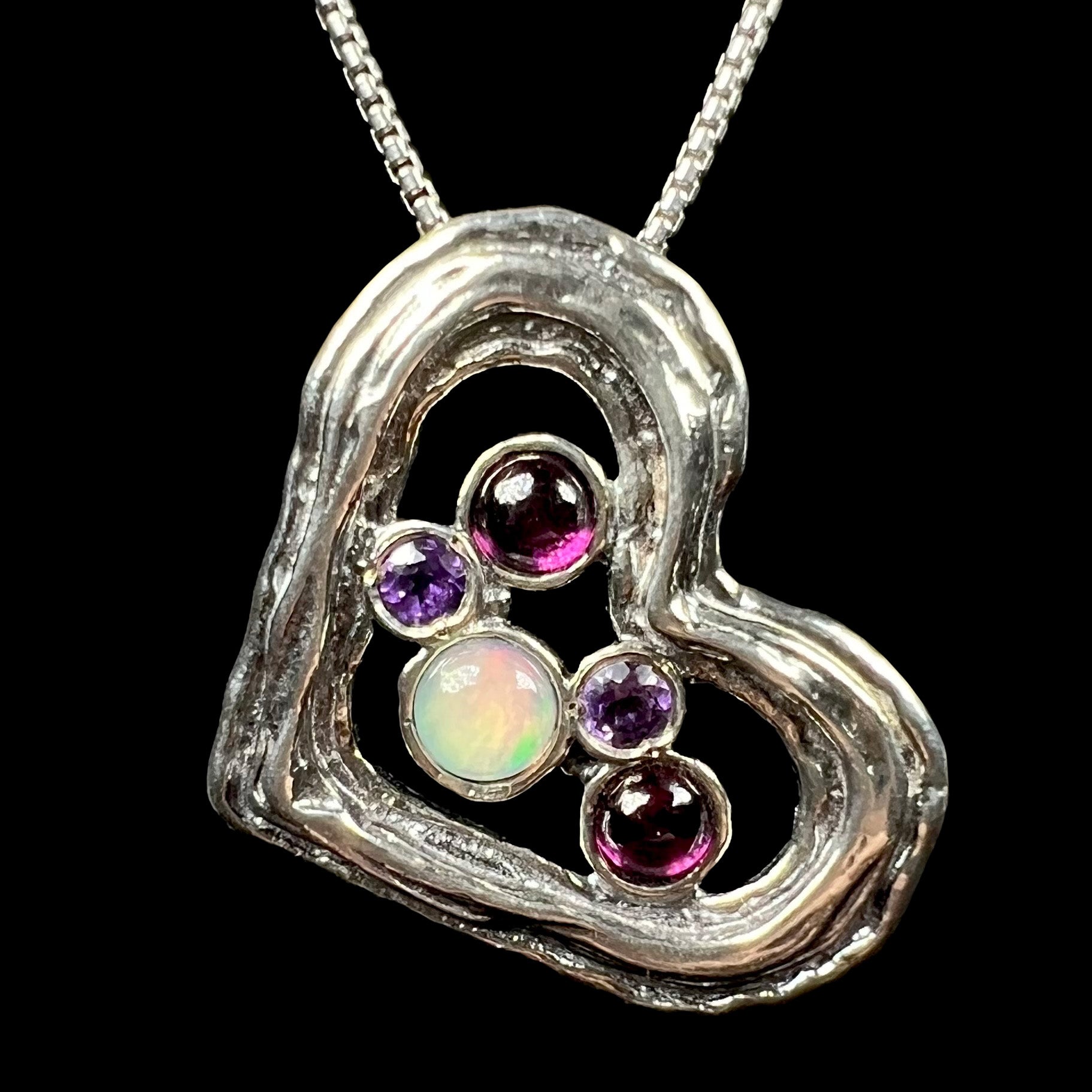 A sterling silver heart necklace set with a round Ethiopoian opal, two amethysts, and two rhodolite garnets.
