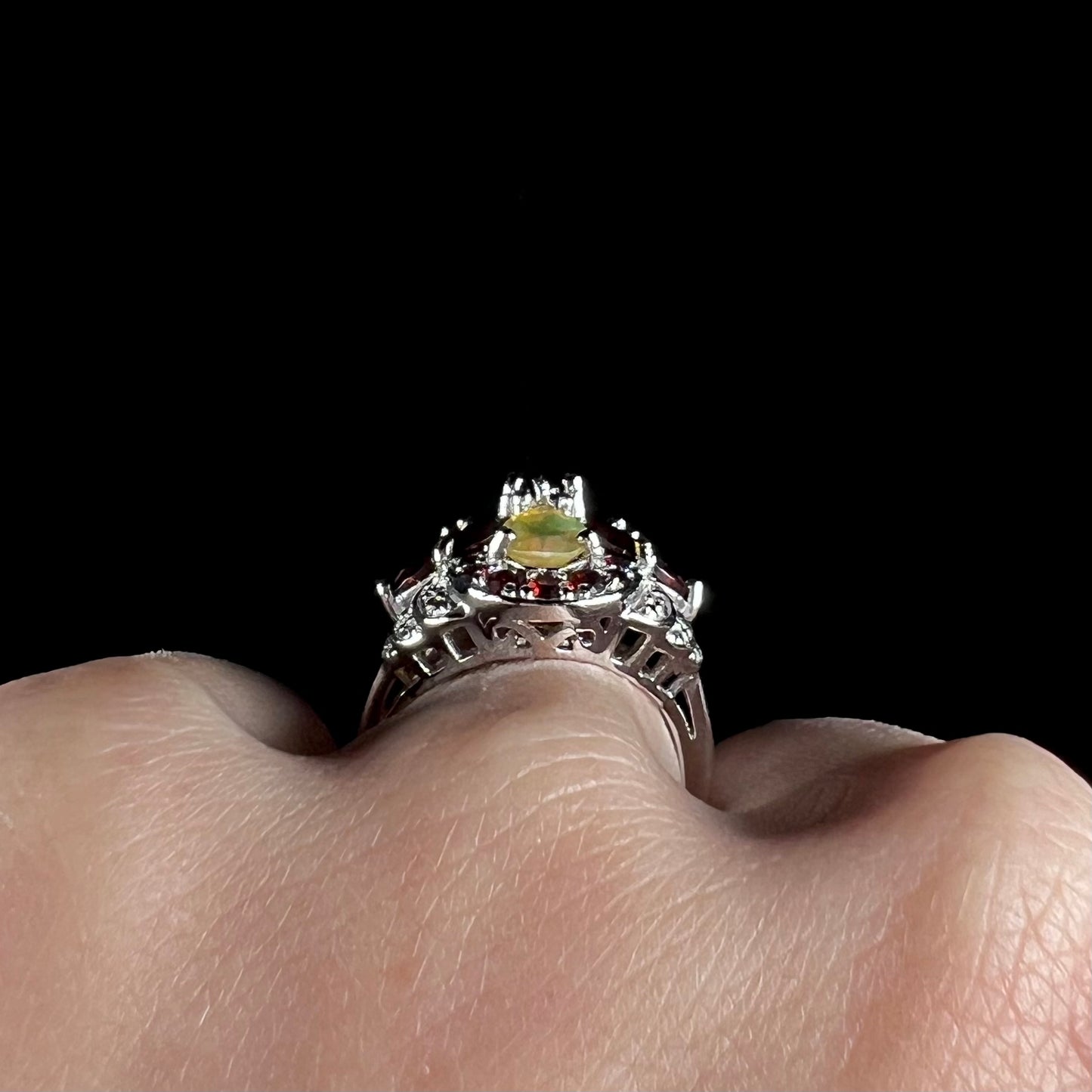 Side gallery view of a sterling silver Ethiopian opal and garnet infinity-design ring with diamond accents.