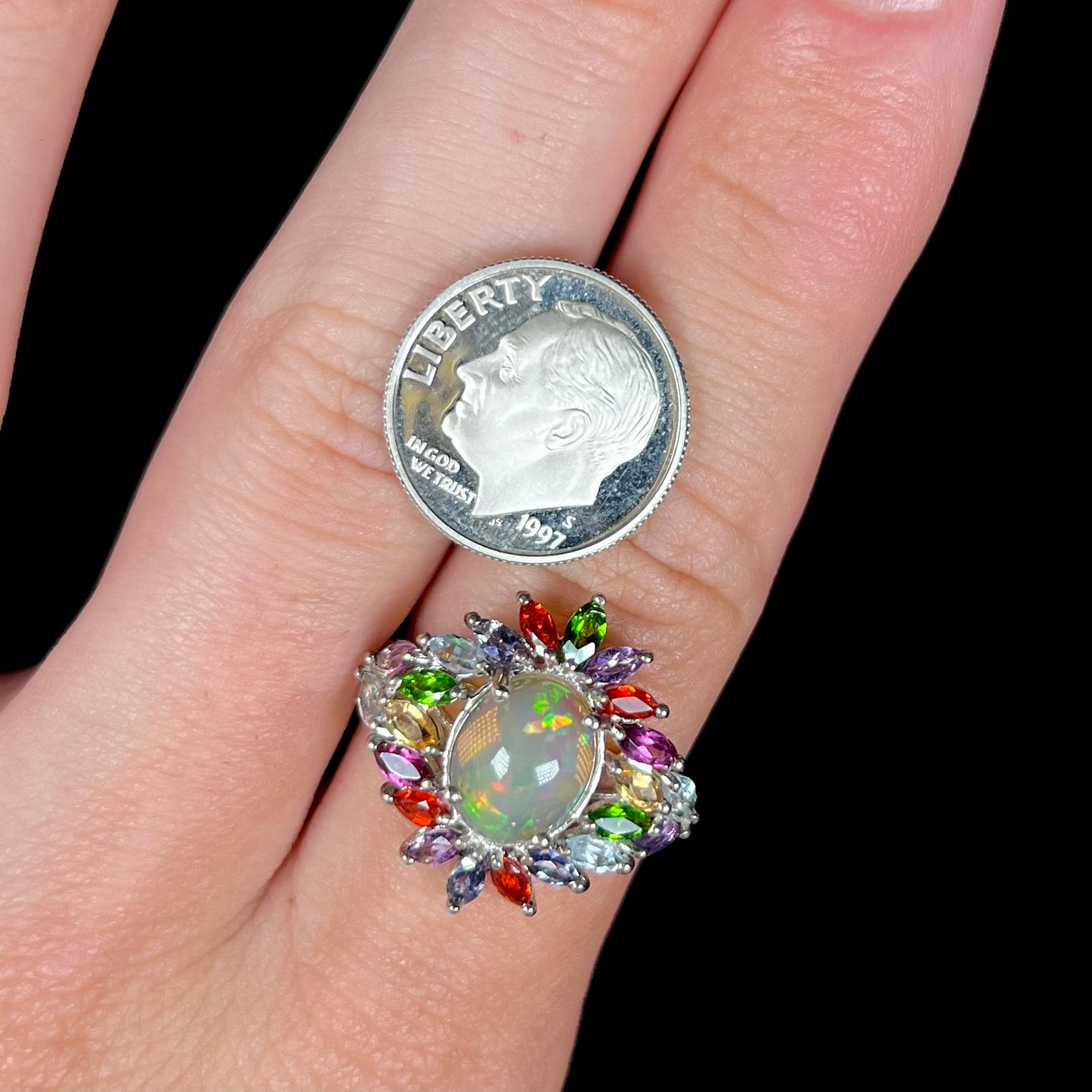 A silver opal multi-gemstone ring worn on finger next to a dime coin for scale.