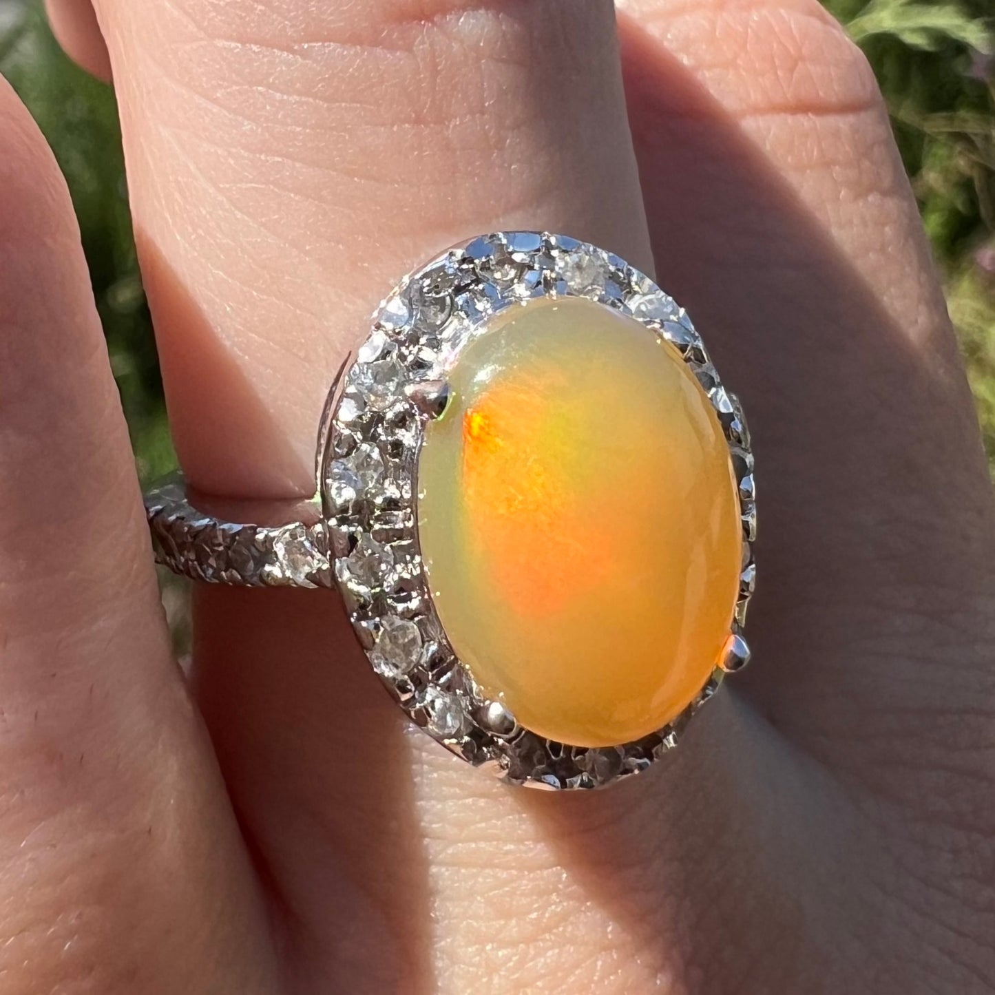 A sterling silver Ethiopian fire opal ring with a CZ halo worn at an angle on a hand in natural light.
