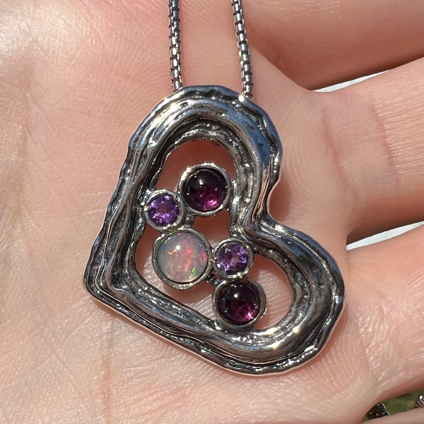 A sterling silver heart necklace set with a round Ethiopoian opal, two amethysts, and two rhodolite garnets.