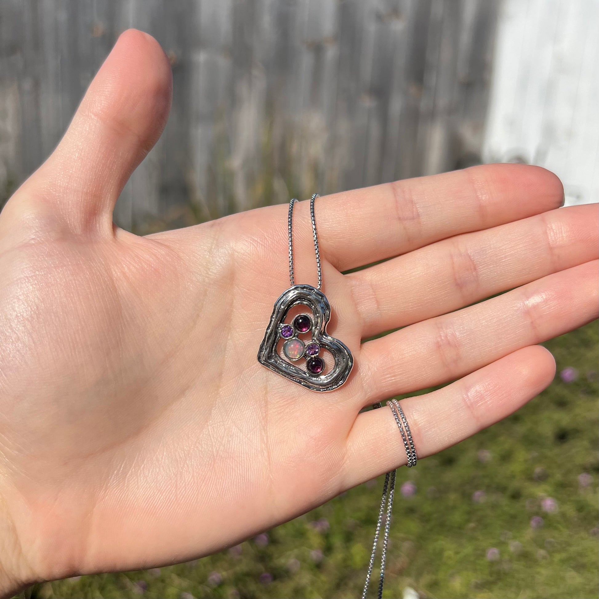 A sterling silver heart necklace set with a round Ethiopoian opal, two amethysts, and two rhodolite garnets.