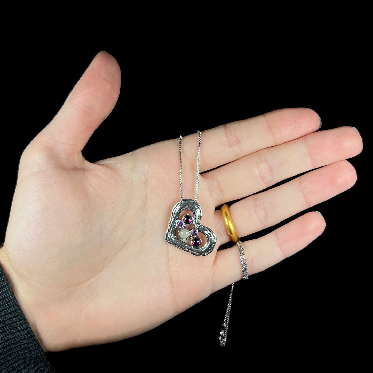 A sterling silver heart necklace set with a round Ethiopoian opal, two amethysts, and two rhodolite garnets.