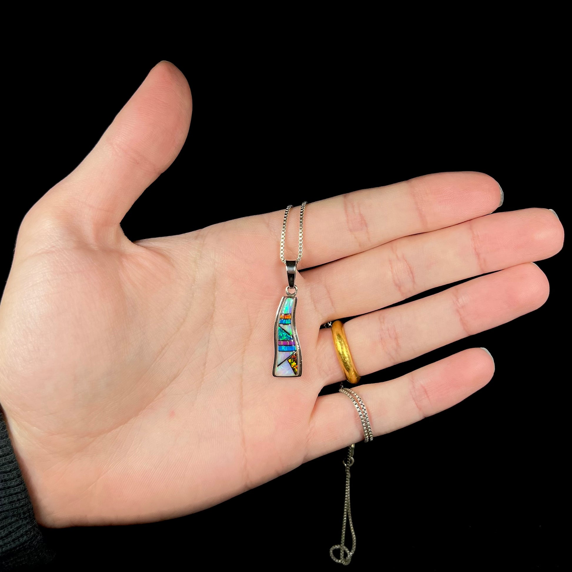 A sterling silver synthetic opal inlay necklace held in a hand against a black background.