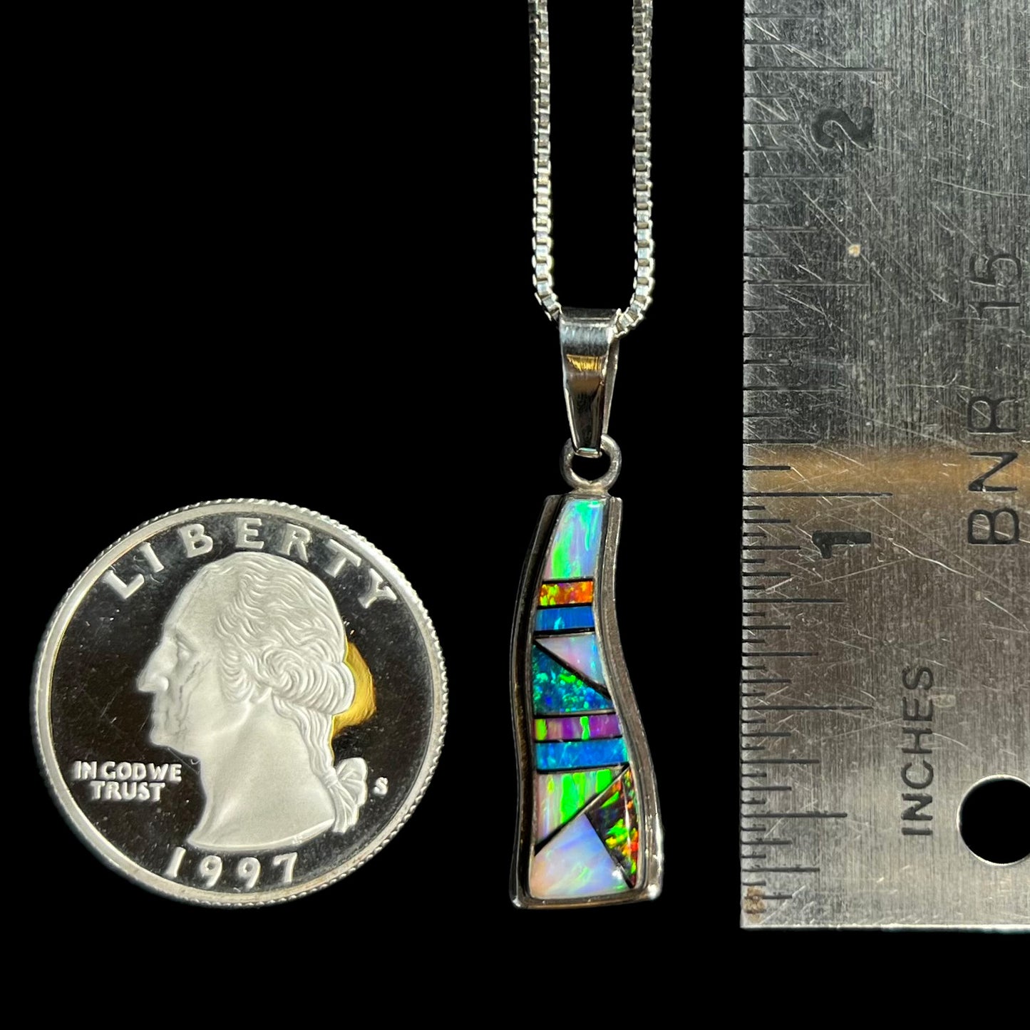 A sterling silver lab-created opal inlay necklace, shown next to a quarter and ruler.  The pendant is 1.5 inches long.