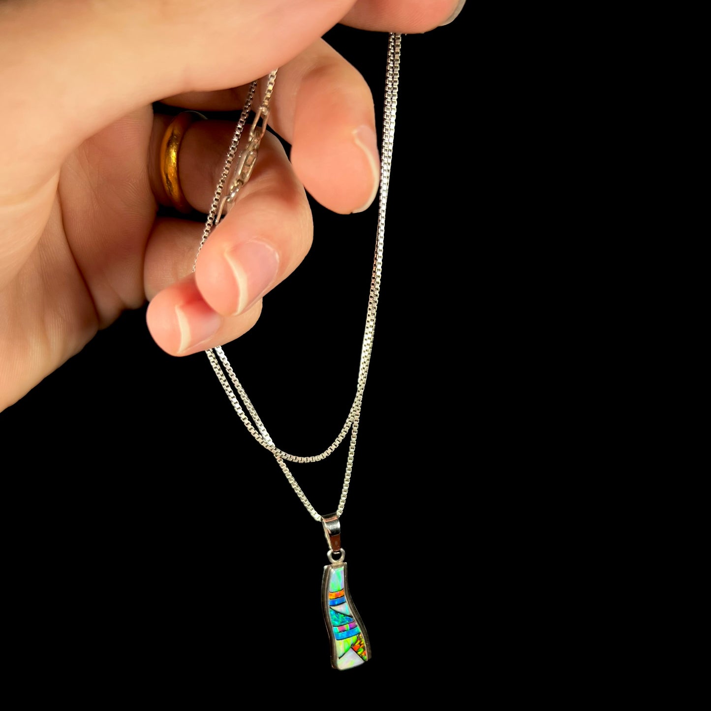 A sterling silver lab-created opal inlay necklace held from the chain by a hand.