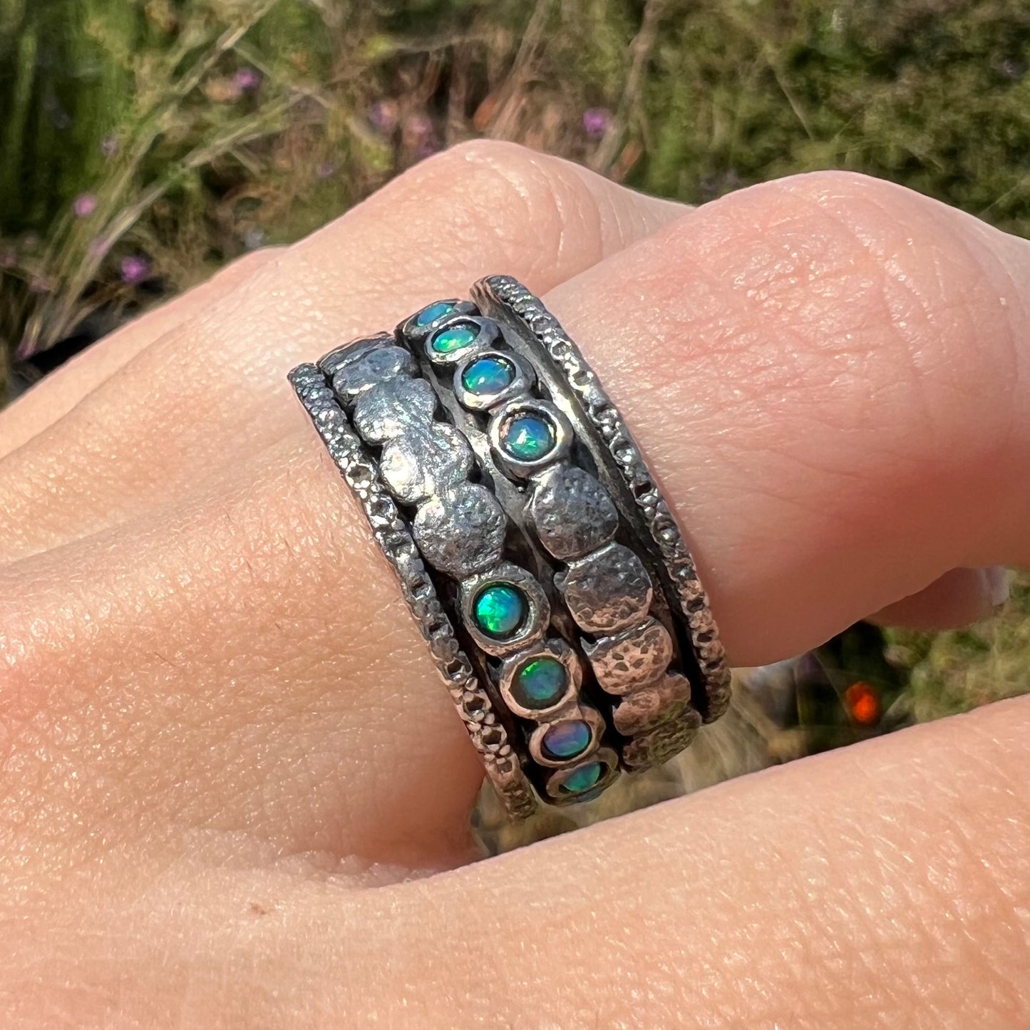 A sterling silver opal men's ring measuring 11.5mm wide, worn on a finger in sunlight outdoors.