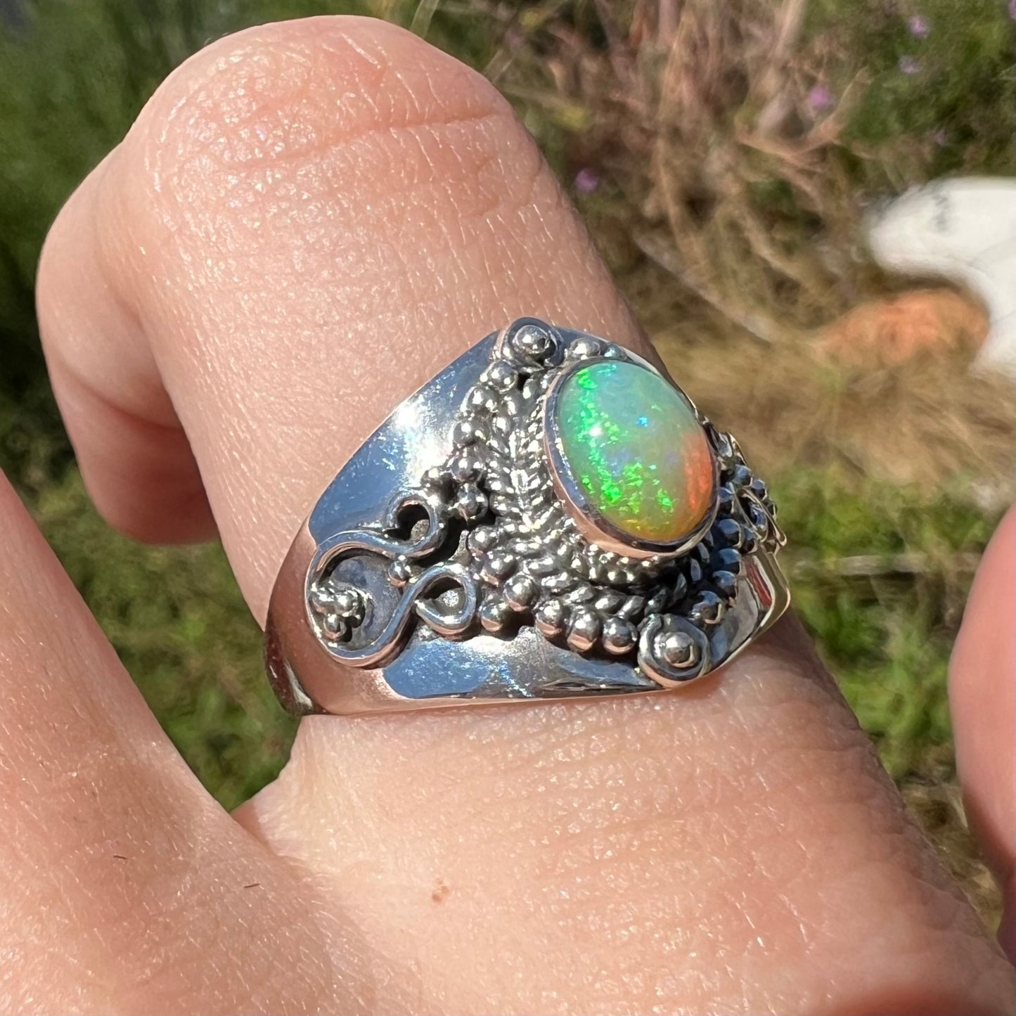 A sterling silver opal men's ring in the sunlight at an angle; the Ethiopian opal plays green fire.