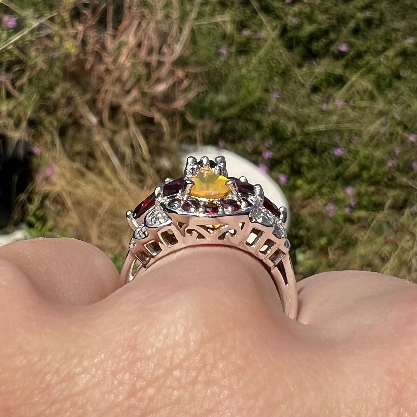 Gallery profile view of a silver opal and garnet ring shown on a hand in outdoor light.