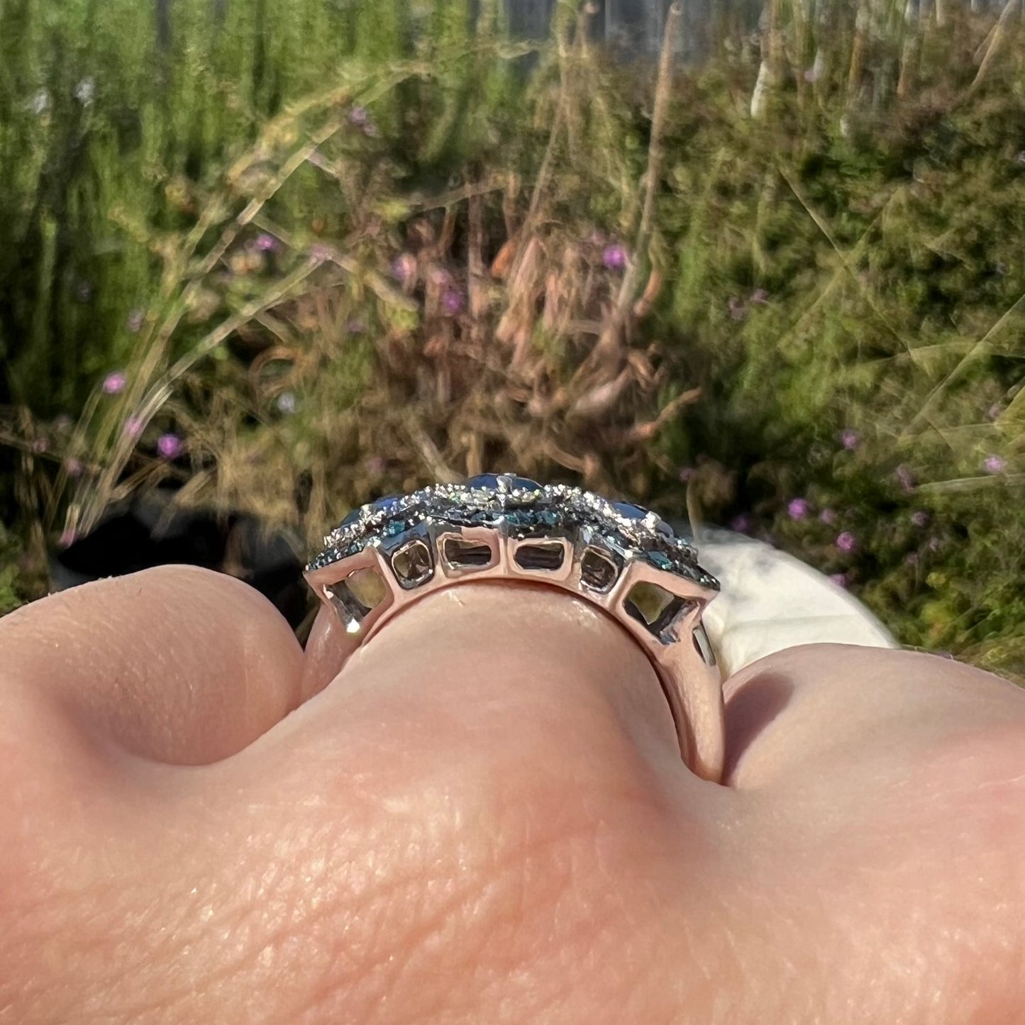 Side gallery profile view of a silver opal ring worn on a finger outside in the light.