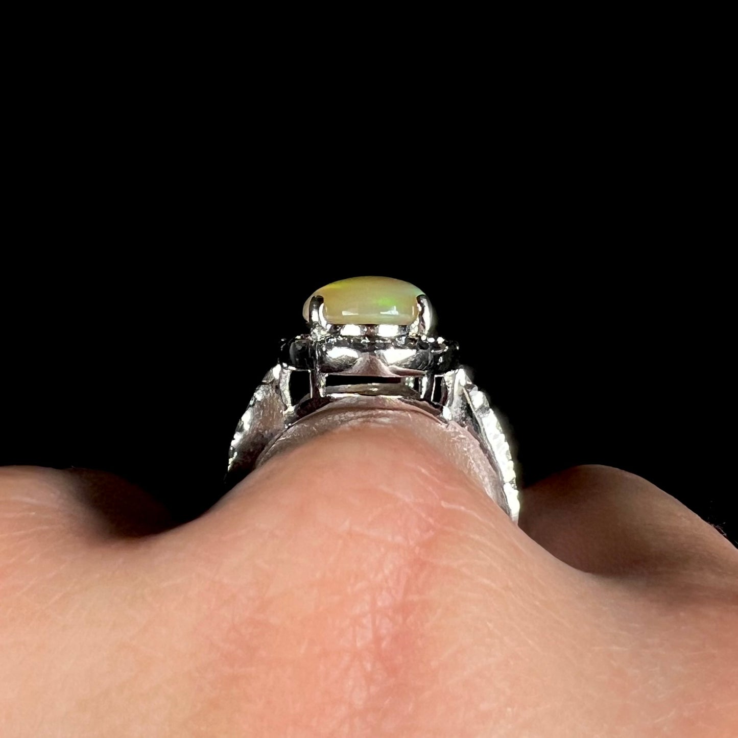 Side profile gallery view of a silver fire opal halo ring on a hand against a black background.
