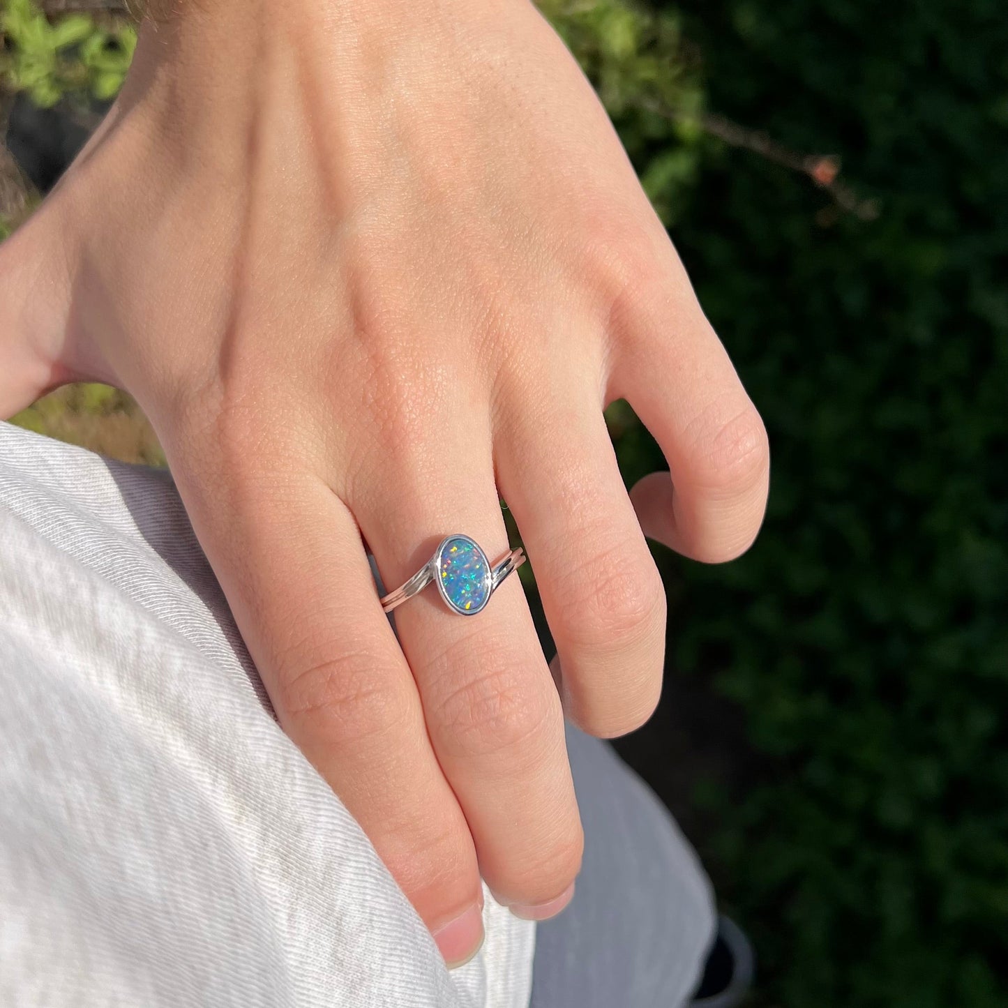A sterling silver ring bezel-set with an oval shaped black opal doublet. The opal has red and blue fire.
